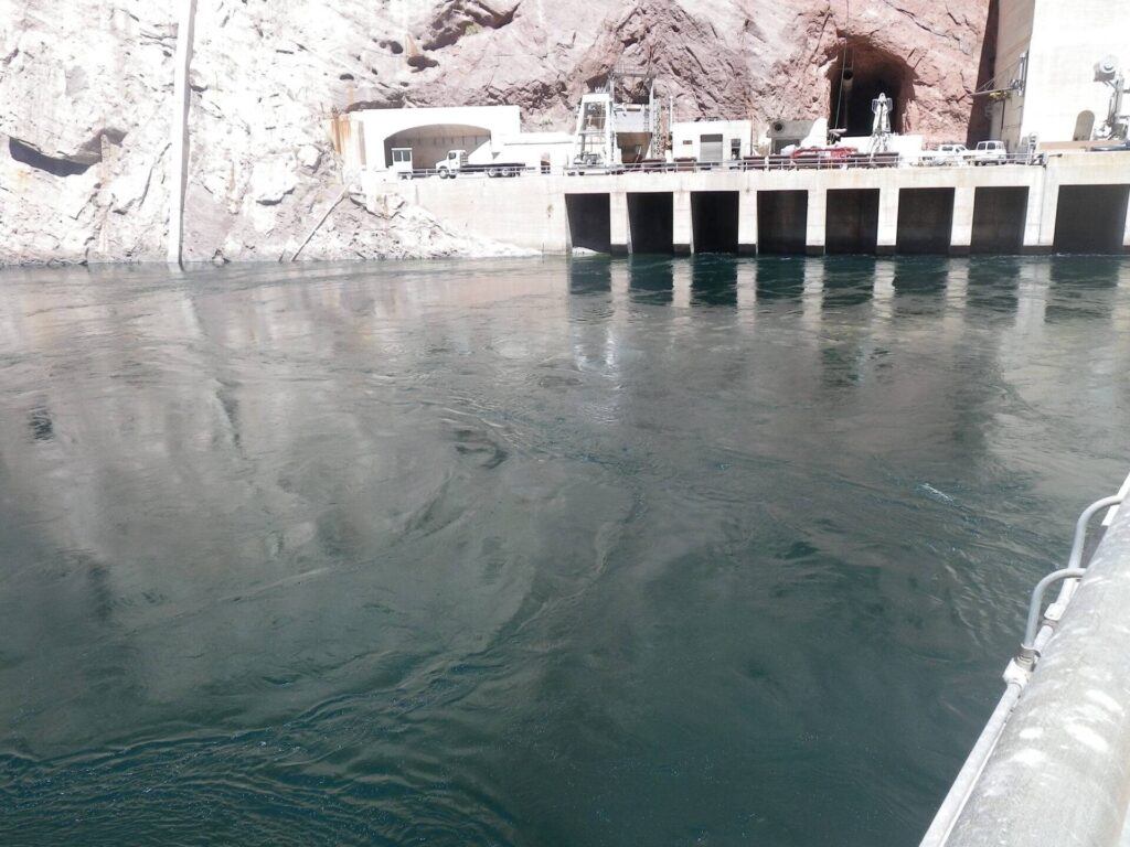 This image illustrates a concrete hydroelectric dam with prominent water intakes and supporting infrastructure set into a rocky cliff.