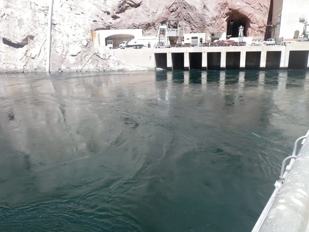 This image illustrates a concrete hydroelectric dam with prominent water intakes and supporting infrastructure set into a rocky cliff.