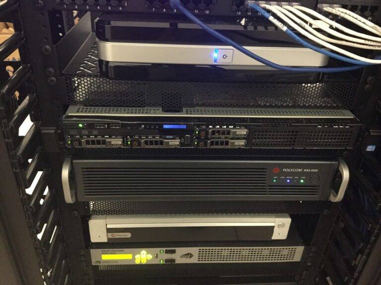 A close-up view of a server rack with various network equipment, including servers and switches, neatly connected with organized network cables. Multiple indicator lights are illuminated on the devices.
