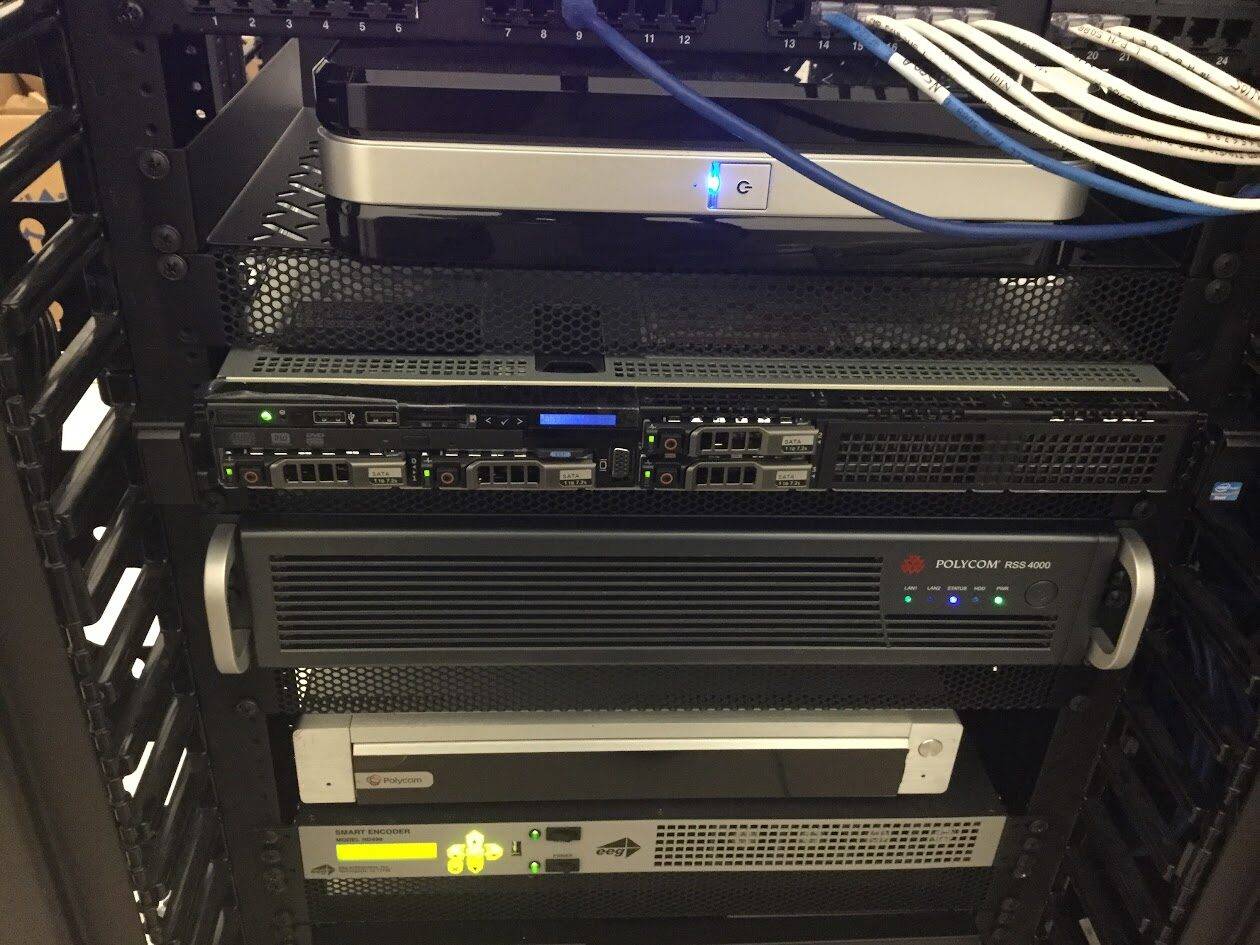 A close-up view of a server rack with various network equipment, including servers and switches, neatly connected with organized network cables. Multiple indicator lights are illuminated on the devices.