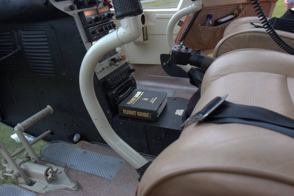 A close-up view of a helicopter cockpit interior, showing tan leather seats, flight controls, instrument panels, and a 