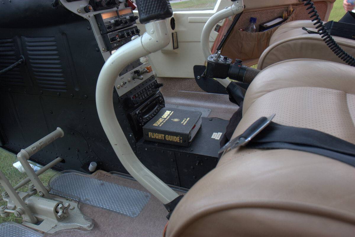 A close-up view of a helicopter cockpit interior, showing tan leather seats, flight controls, instrument panels, and a 