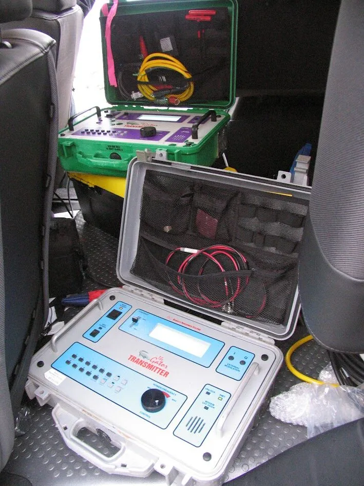 As seen above, two portable testers—one blue "Transmitter" and one green unit—are arranged among wires on a vehicle floor.