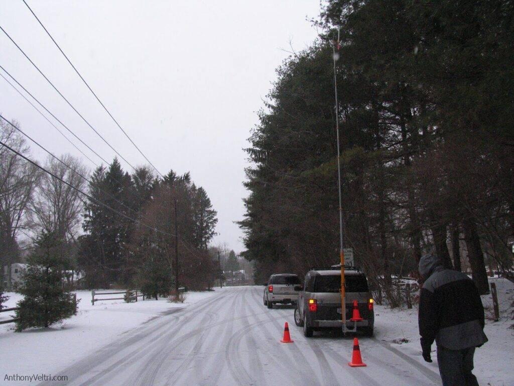 This scene illustrates a rural roadway in winter, with safety markers and nearby pedestrian activity amid snowy conditions.
