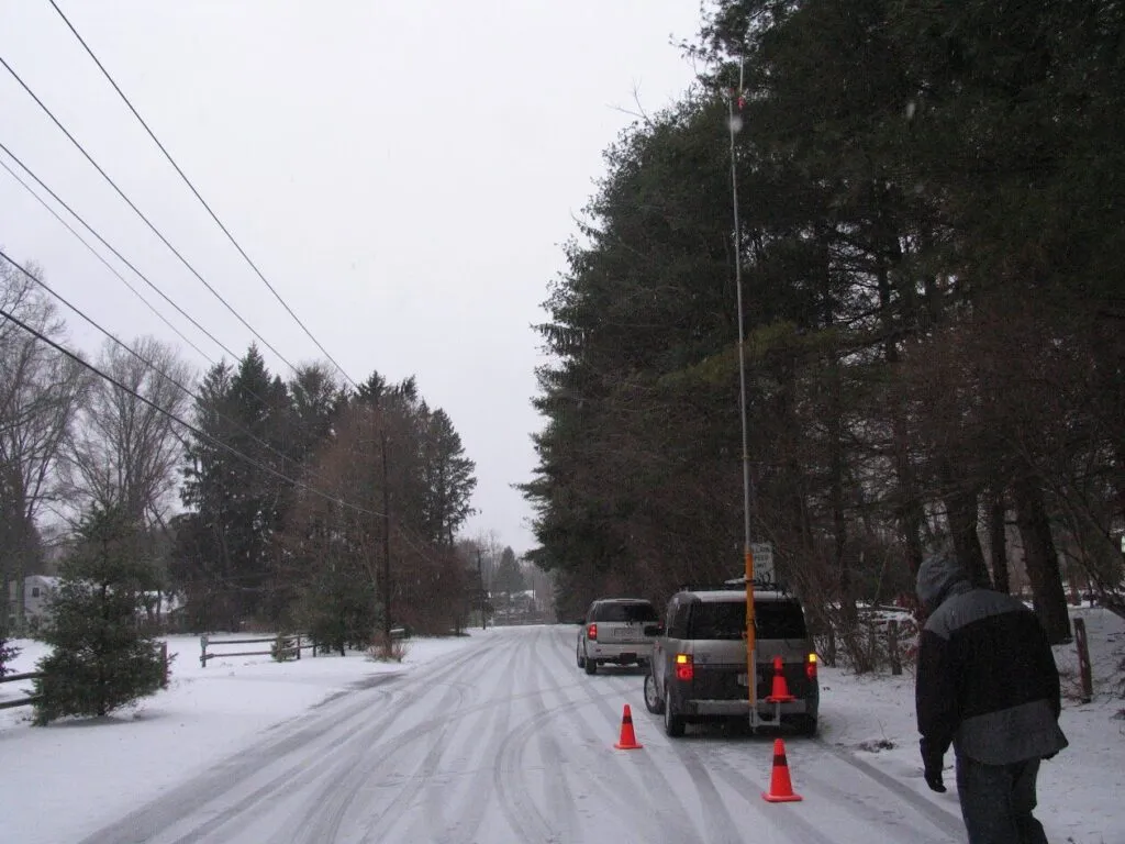 This scene illustrates a rural roadway in winter, with safety markers and nearby pedestrian activity amid snowy conditions.
