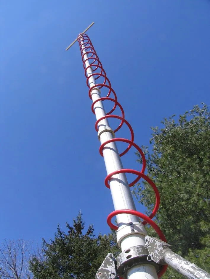 This image illustrates the structure of a white antenna pole with a red helical coil, emphasizing vertical scale and outdoor context.
