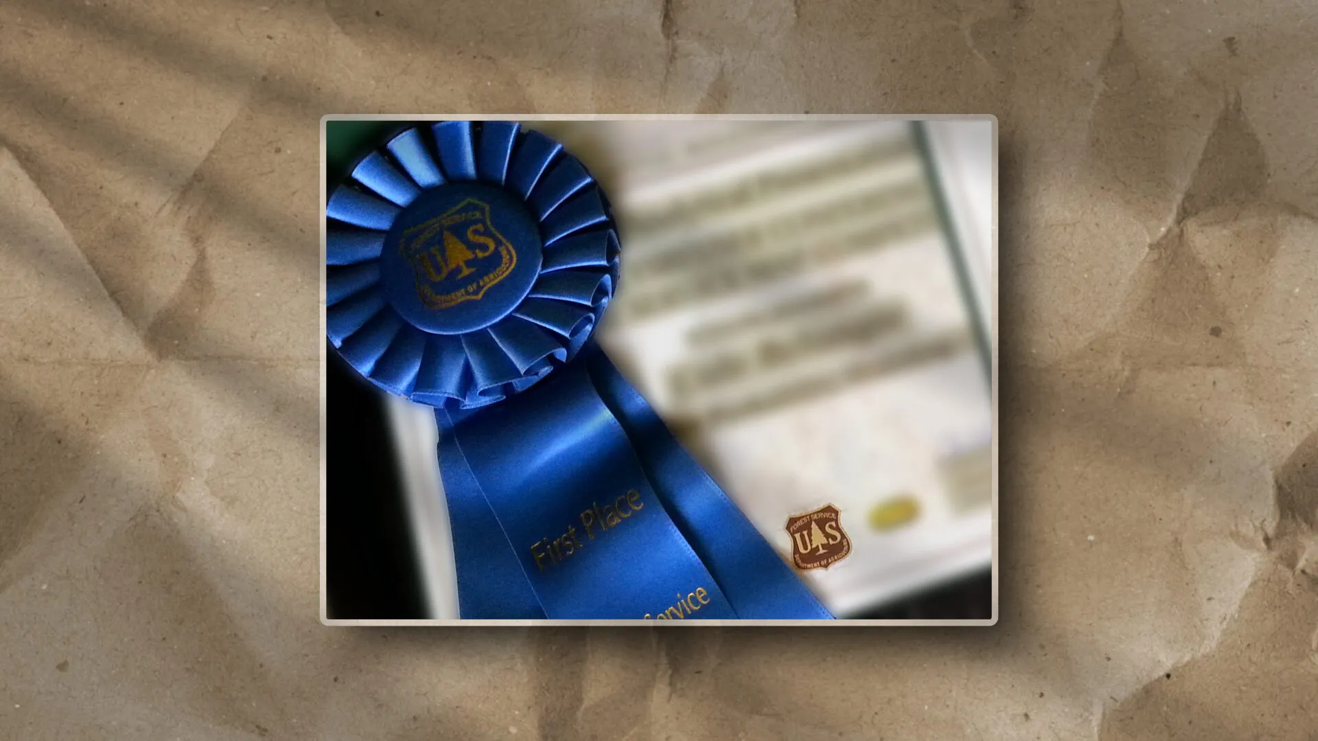 This image features a U.S. Forest Service award ribbon over an indistinct certificate, suggesting recognition of achievement.