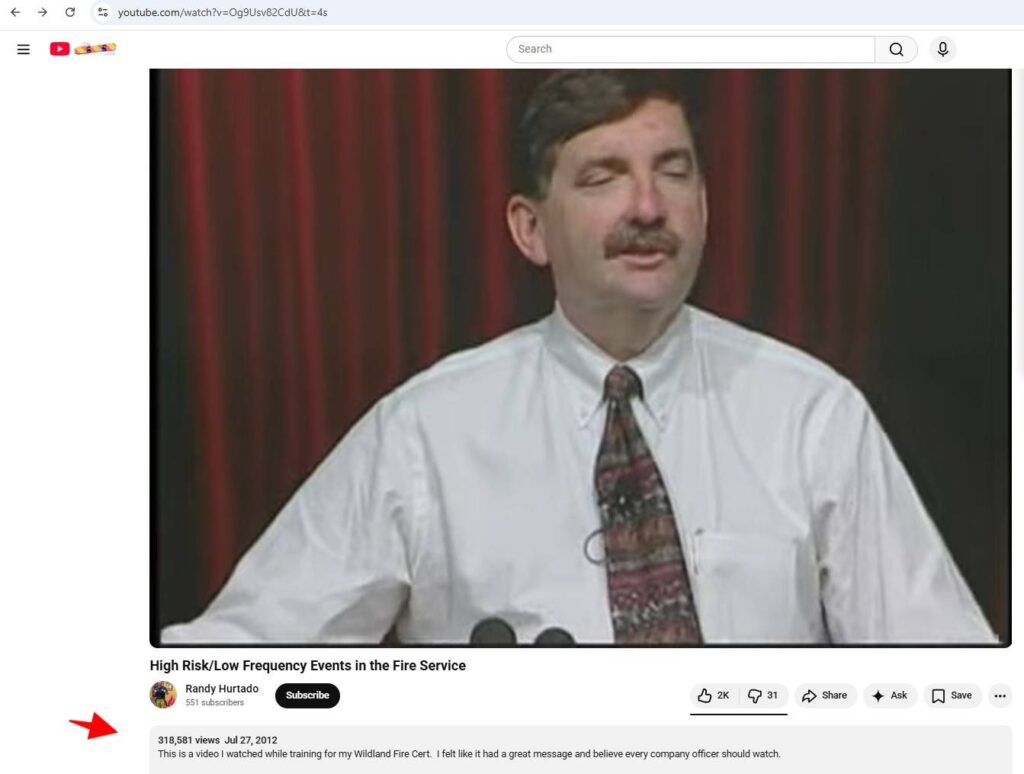 A man with a mustache in a white shirt and patterned tie stands giving a speech, with red and black vertical curtains in the background. The YouTube video is titled "High Risk/Low Frequency Events in the Fire Service" by Randy Hanifen.