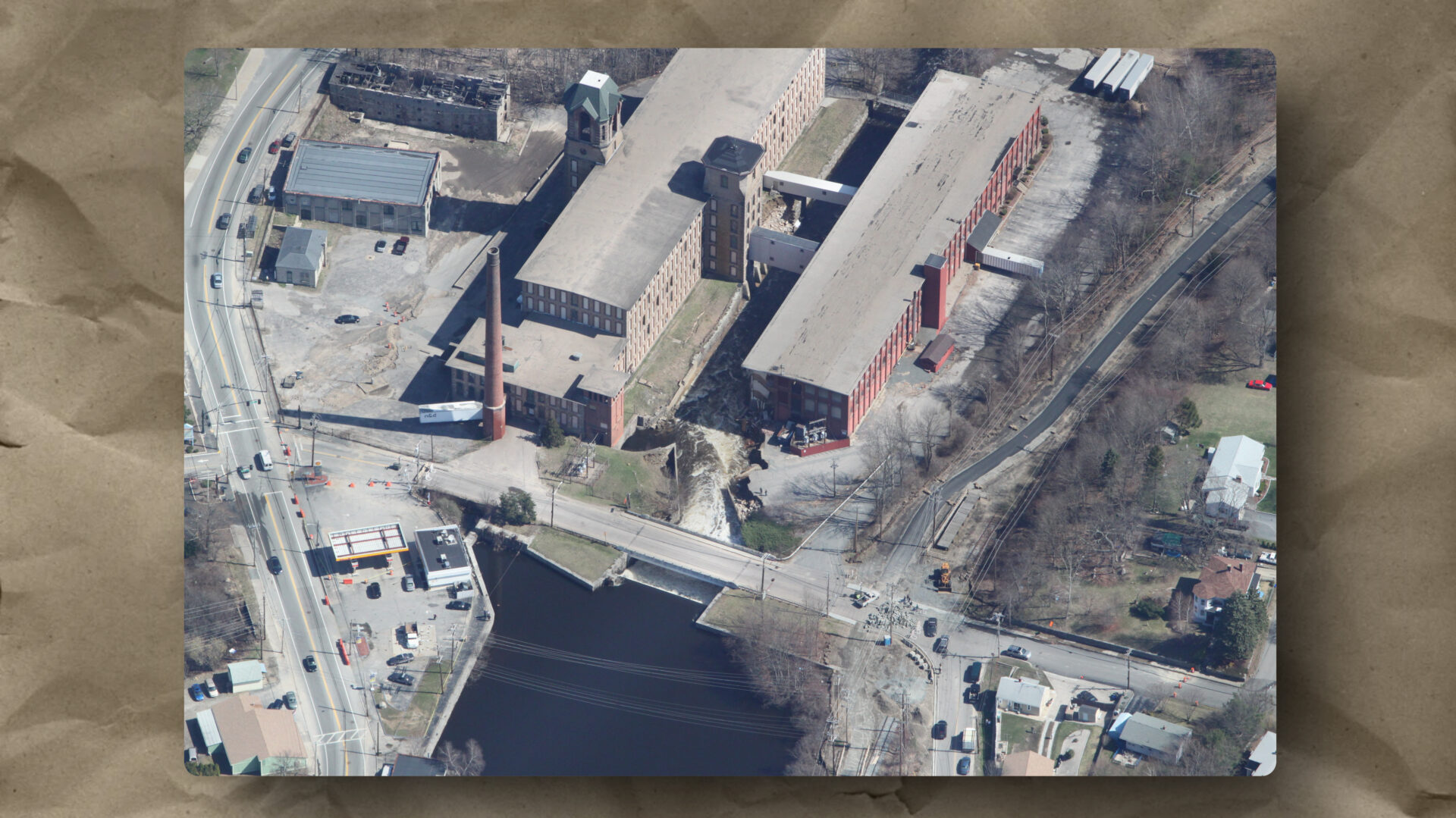 Arctic Mill complex, South Branch of the Pawtuxet River, West Warwick, Rhode Island, April 2010. The Pawtuxet River crested nearly thirteen feet above flood stage on March 31, 2010. The dam that once powered production has failed. The paved surface and building corner at center are washing into the river. The physical system fails. The community built around it absorbs the consequences. Photograph by Anthony Veltri.